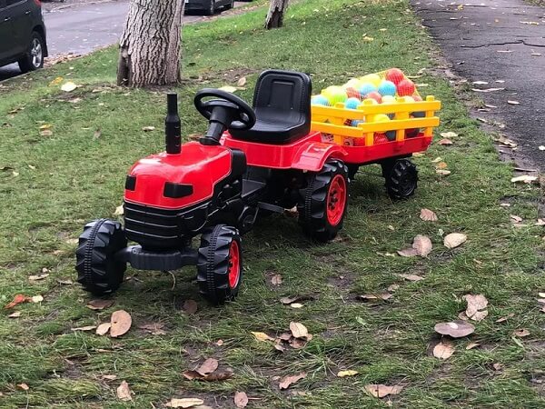 Traktor za decu Biberoglu crvene boje na pedale sa prikolicom, prikazan u realnom ambijentu